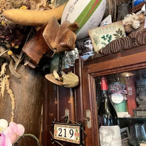 Assortiment éclectique d'objets, dont un ballon de rugby marqué 'Maison Saint Dominici', une ancienne forme à chaussure en bois, une plaque métallique numérotée '219', une bouteille de vin, et divers autres objets décoratifs et vintage sur un fond en bois.